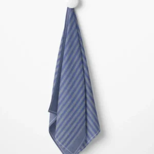 Ein Grubentuch blau gestreiftes Küchentuch hängt an einem weißen runden Haken an einer schlichten weißen Wand.