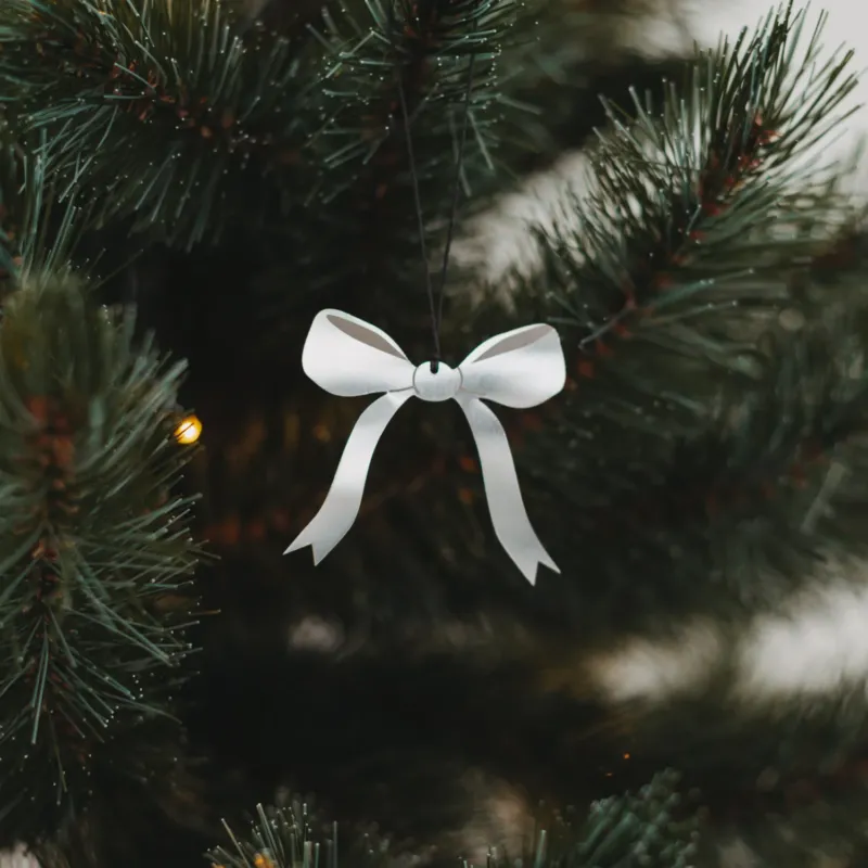 Silberner Schleifenanhänger aus Metall am Weihnachtsbaum mit Lichterkette, stilvoll und festlich dekoriert.